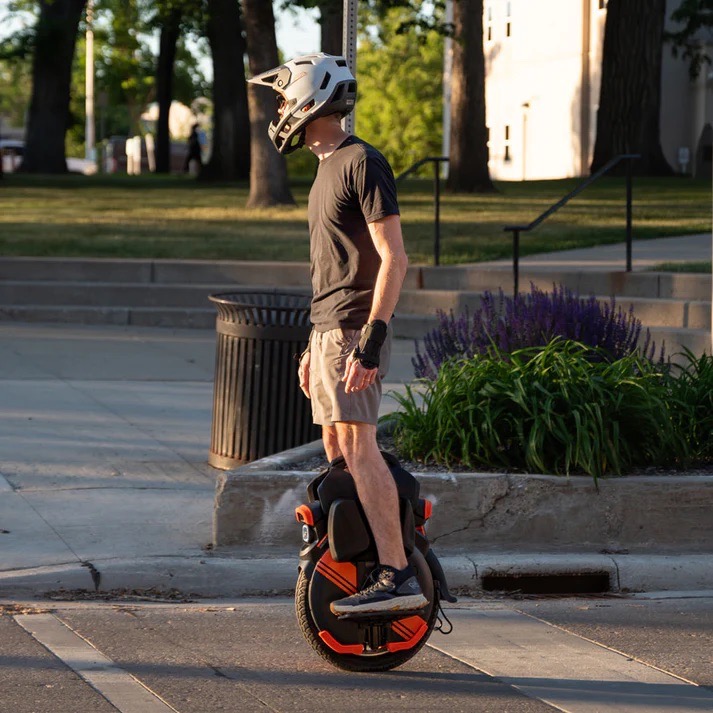 Side view of a man commuting on an Inmotion V11Y electric unicycle, wearing a helmet and wrist guards.