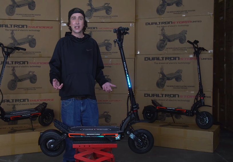 Electric scooter Dualtron spider 2 video thumbnail where a man is standing behind the scooter.