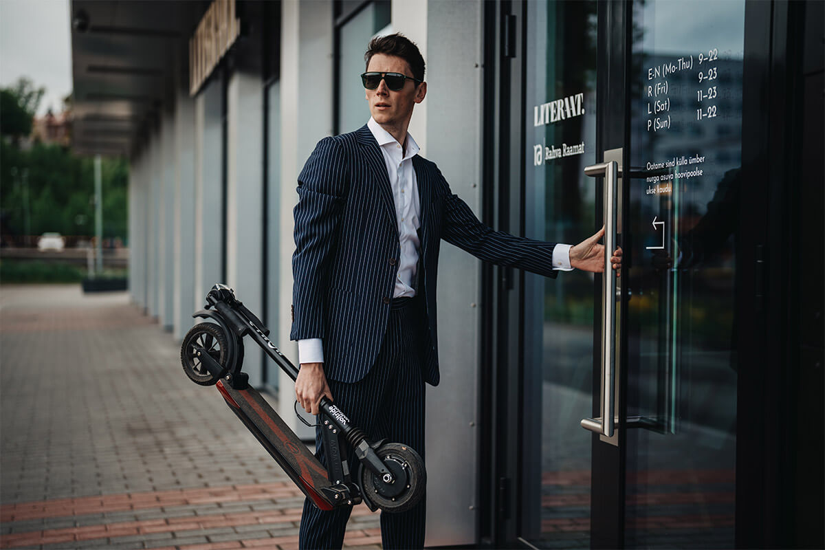 Man in business suit carrying folded E-TWOW S2 ECO electric scooter – ideal for commuting and portability.