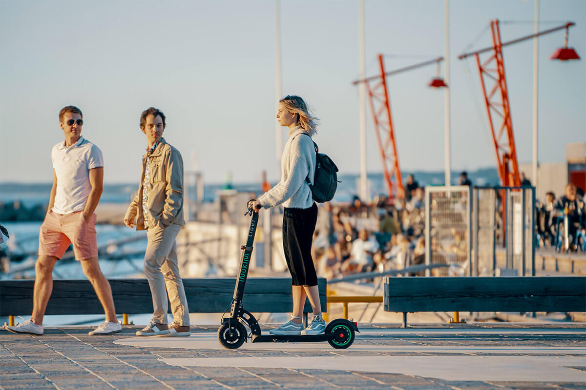 Woman riding the INOKIM Light Hero electric scooter along a marina path, combining style and performance.