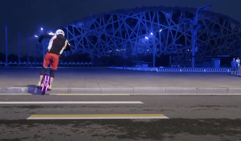 Rider performing night-time curb jump on Kingsong KS-16X electric unicycle with colorful LED lights