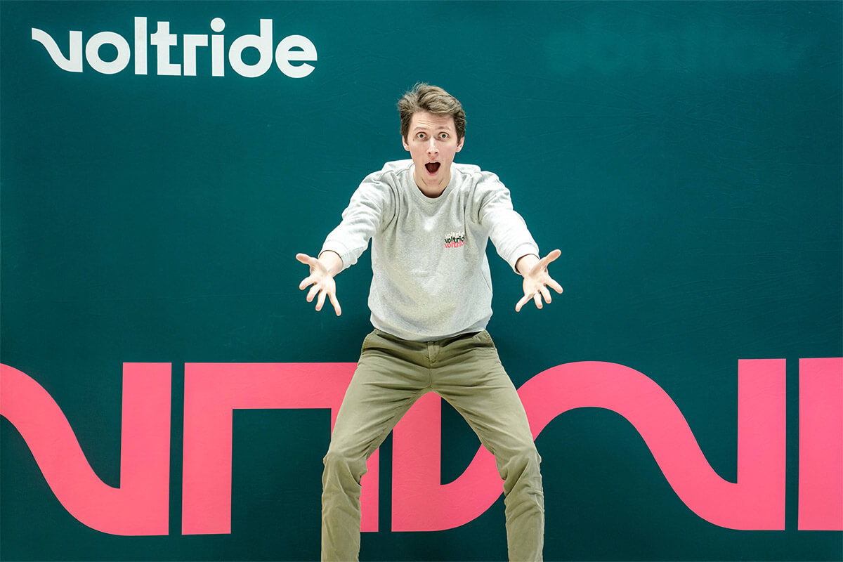 Voltride about us after sales support Enthusiastic man posing playfully in front of a colorful Voltride backdrop, arms outstretched and expression full of excitement.