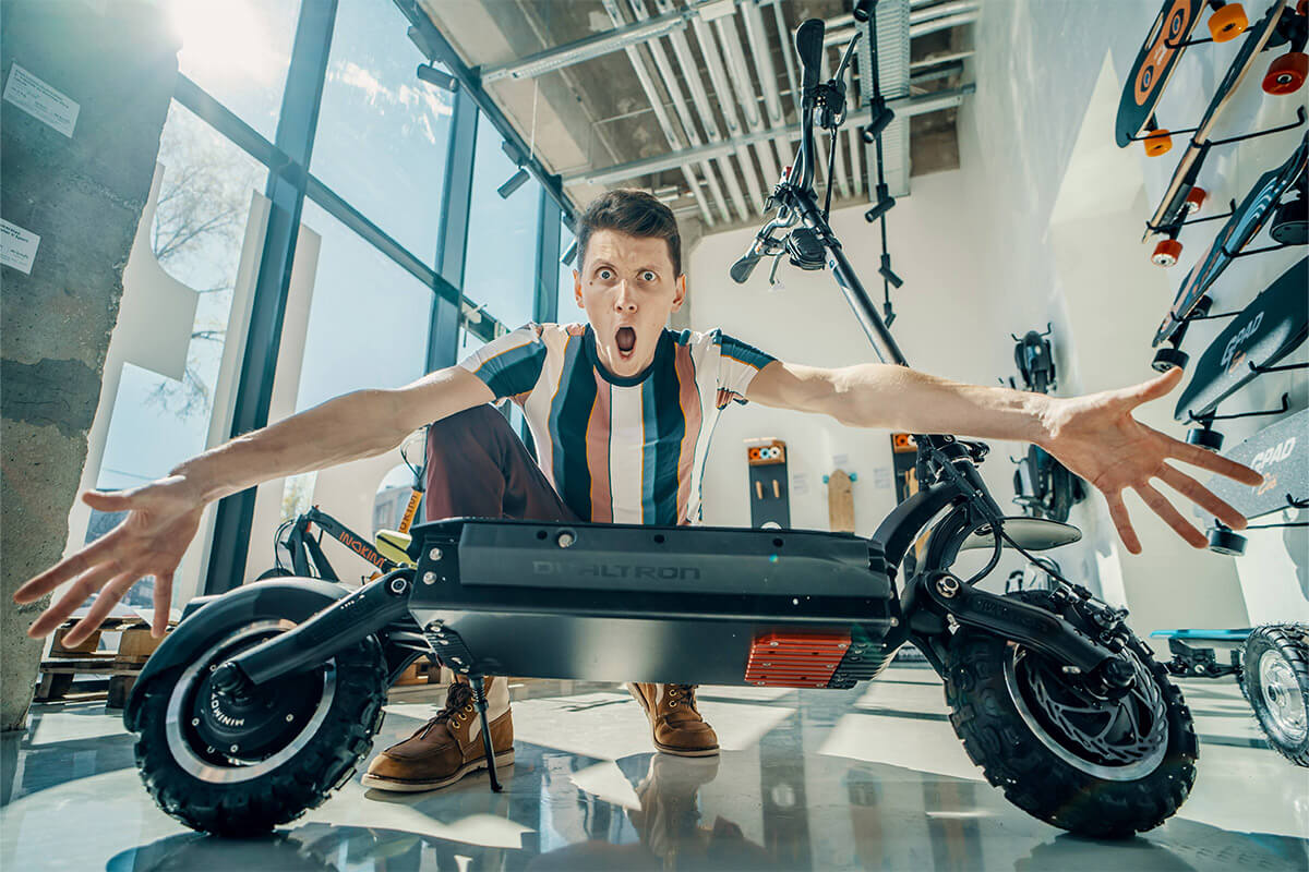 Excited man posing dramatically with a powerful Dualtron electric scooter inside a Voltride showroom filled with micromobility gear.