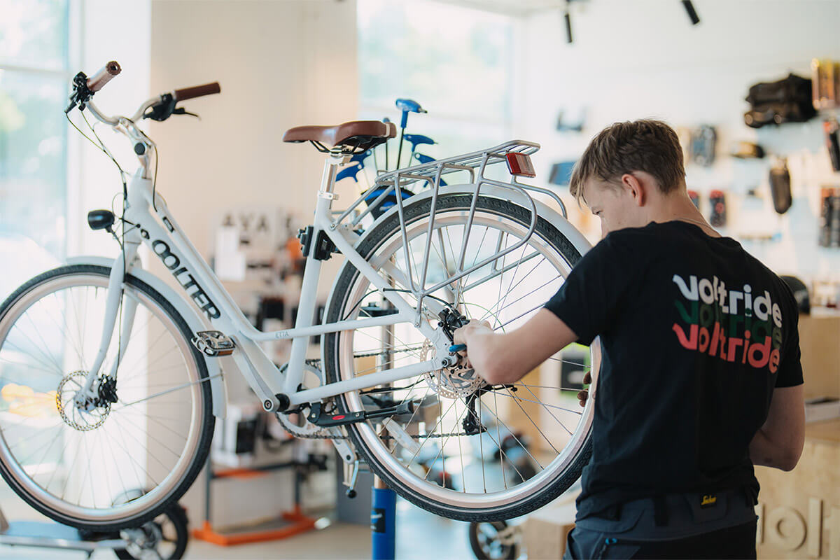 Voltride technician servicing the rear wheel of a white electric bicycle inside a bright and modern repair workshop.