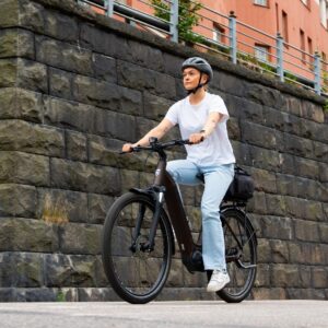 Close up view of a young woman riding the Tunturi eHybrid low-step electric bicycle on the city streets wearing a helmet.