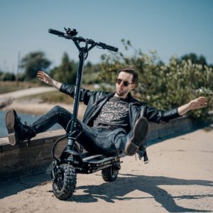 Man sitting casually on Dualtron Ultra 2 electric scooter at the beach, showcasing rugged off-road design and laid-back lifestyle