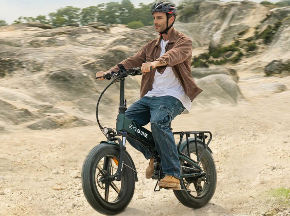A man wearing a helmet riding the green Engwe Engine PRO 2.0 fat-tire electric bicycle across a sandy, rocky outdoor trail.