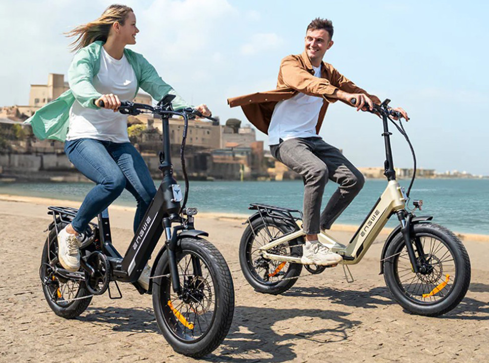 A man and a woman riding the Engwe L20 3.0 Boost electric bicycles on a city seashore on a sunny day.