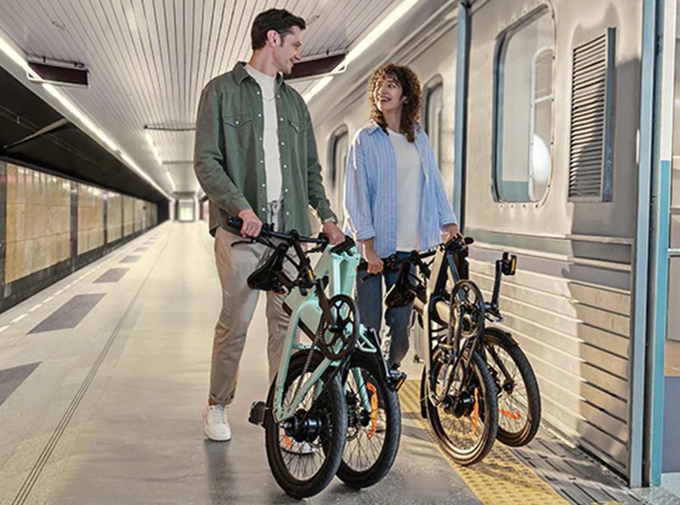 Man with folded mint Engwe P20 and woman with folded black Engwe P20 electric bike in the train station