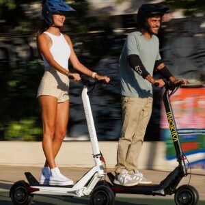 Man and a woman riding the Inokim OX electric scooters on the city street wearing helmets.