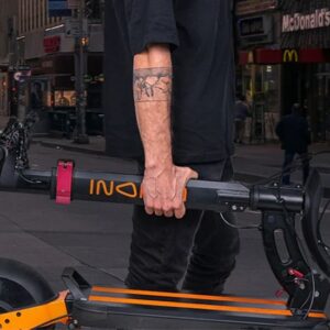 Man carrying the Inokim Quick 4 electric scooter on the city street.