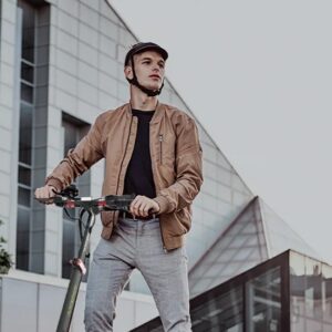Man standing with the Inokim Light 2 electric scooter on the city street wearing a helmet.