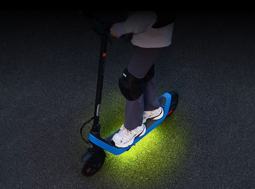 Kid standing on the Segway-Ninebot C2 Lite Kids electric scooter with the RGB colors lit.