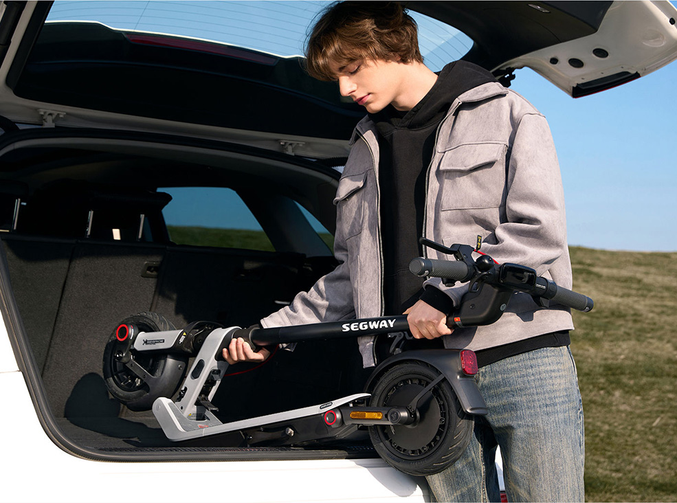 Person loading a folded Segway-Ninebot E3 Pro E electric scooter into the trunk of a car, illustrating the scooter’s compact and portable design.