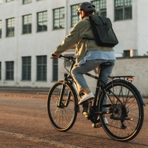 Rear side view of a woman riding a Tunturi eMotion electric bicycle on the city streets wearing a helmet.