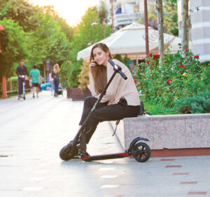 Woman sitting next to the E-TWOW S2 Booster Plus electric scooter on the city street.