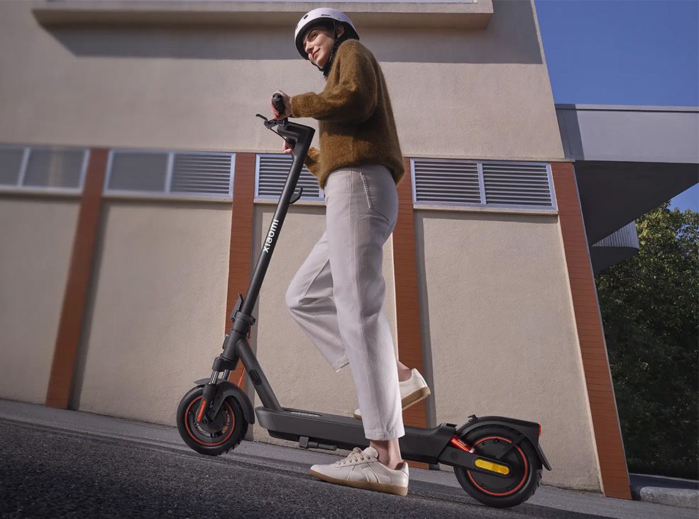 Xiaomi 5 Max slope parking system Person wearing a helmet riding the Xiaomi 5 Max electric scooter uphill demonstrating the scooter's slope parking system on a city street in daylight.