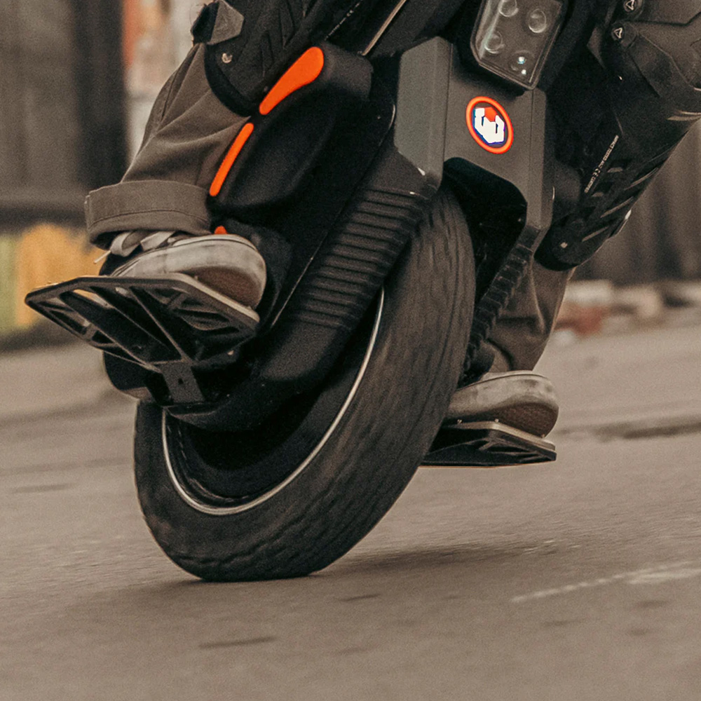 Close-up of a rider carving on the Inmotion V12S electric unicycle, showing the tilted wheel, pedals, and rugged footgear in motion on the street.