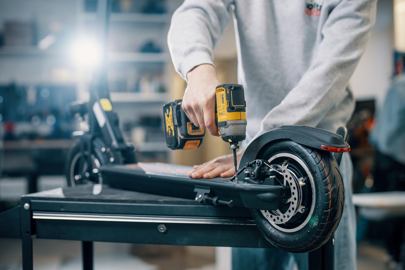 A technician uses a power drill to repair the rear section of an electric scooter placed on a workbench in a workshop.
